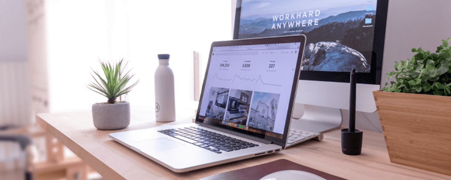 Home-Office-Arbeitsplatz mit Macbook und iMac, auf Desktop der Schriftzug “Work hard anywhere”.